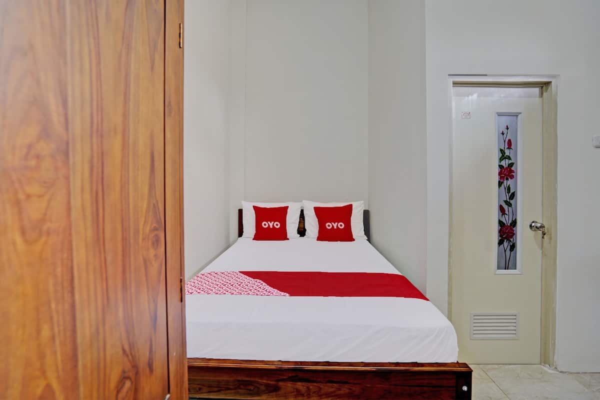 Una cama bien hecha con ropa de cama roja y blanca, un cabecero de madera y una puerta con un diseño floral.