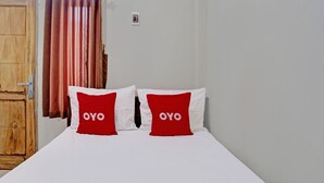 A bed with white sheets and two red pillows with "OYO" text, a wooden wardrobe, and a curtain. - OYO 92541 Suny Kost Syariah (Sidoarjo)