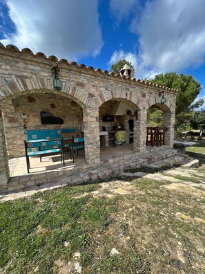 A stone building with a tiled bench and a table, featuring an archway entrance and outdoor seating area. - Masia CAN Tronc Casa Rural Tranquila,disfrutar en la Naturaleza en Familia (BARCELONA)