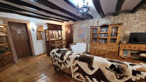 A cozy living room with exposed wooden beams, a stone wall, a fireplace, and a sofa covered with a patterned blanket. - Masia CAN Tronc Casa Rural Tranquila,disfrutar en la Naturaleza en Familia (BARCELONA)