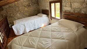 A rustic room with stone walls, wooden beams, and two beds with white bedding. - Masia CAN Tronc Casa Rural Tranquila,disfrutar en la Naturaleza en Familia (BARCELONA)