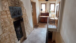 Un pasillo estrecho con una chimenea de piedra, una mesa de comedor de madera con sillas y un ventanal con luz natural.