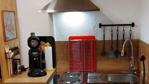 Una cocina compacta con campana de acero inoxidable, un lavamanos y un refrigerador.