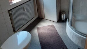 Un baño pequeño con inodoro, ducha y ventana que deja entrar luz natural.