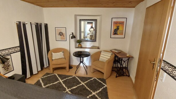 Un espacio habitable compacto con sofá, dos sillones, una mesita redonda y un espejo.