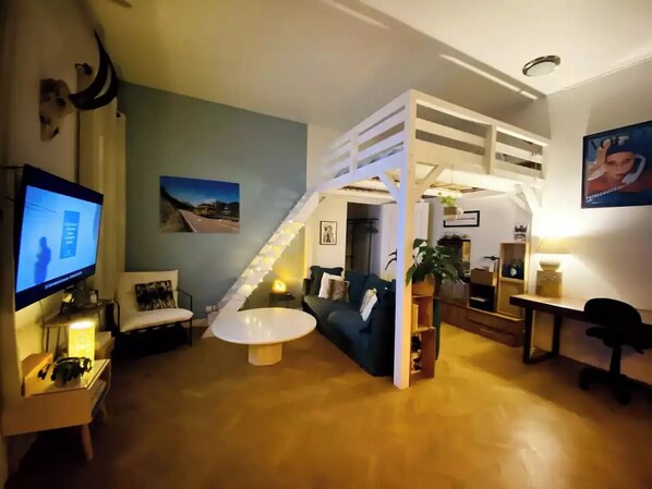 A modern living room with a staircase, a television, a sofa, a coffee table, and a desk with a chair.