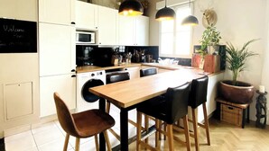 A modern kitchen with white cabinets, a wooden dining table, and pendant lights. - Appartement Design Proche Paris & Versailles (Meudon)