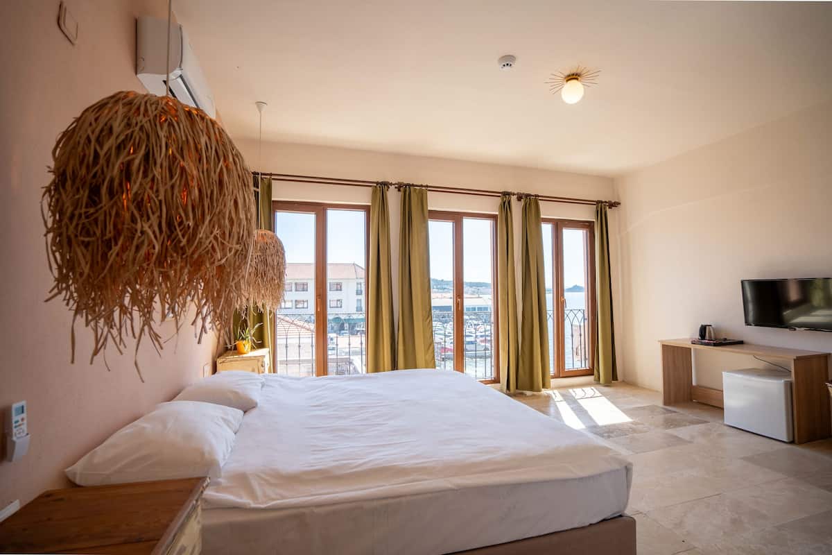 A hotel room with a bed, a desk, a TV, and large windows with curtains.