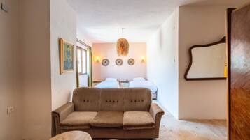 Una habitación de hotel moderna con un sofá marrón, una mesa de centro redonda y una cama con sábanas blancas. Hay luces fijadas a la pared y un espejo.