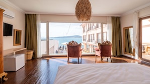 A hotel room with a large bed, two chairs, a TV, and a view of the sea. - Casalyma Ayvalık (Ayvalik)