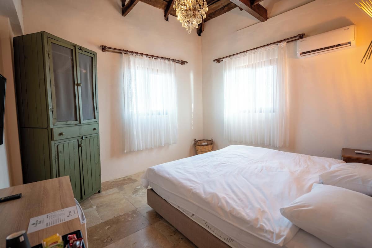 A bedroom with a bed, a wooden table, a green cabinet, and a window with curtains.