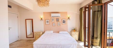 Un dormitorio con una cama grande, una lámpara colgante, aire acondicionado instalado en la pared y una ventana con cortinas.