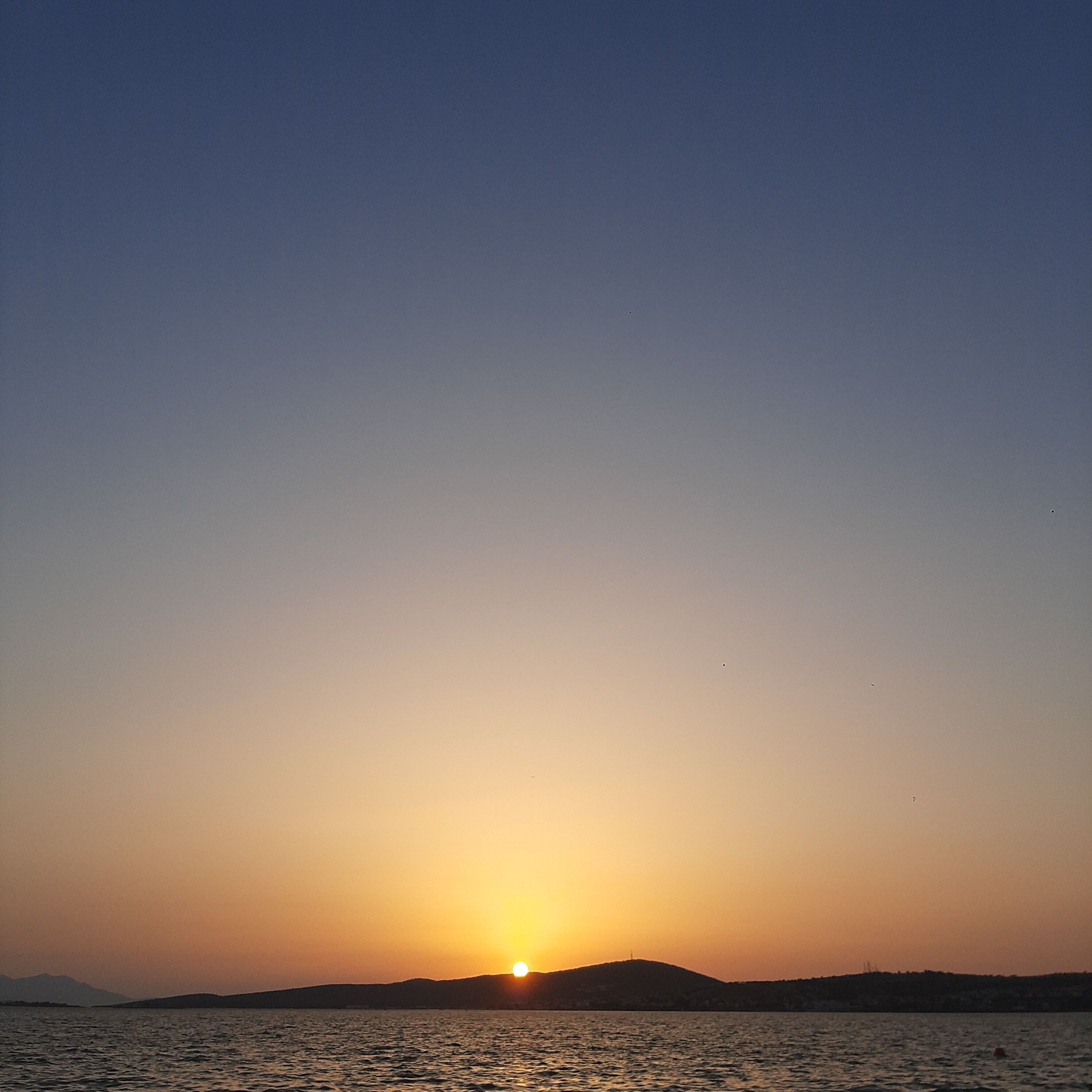 A sunset over a body of water with distant landforms.