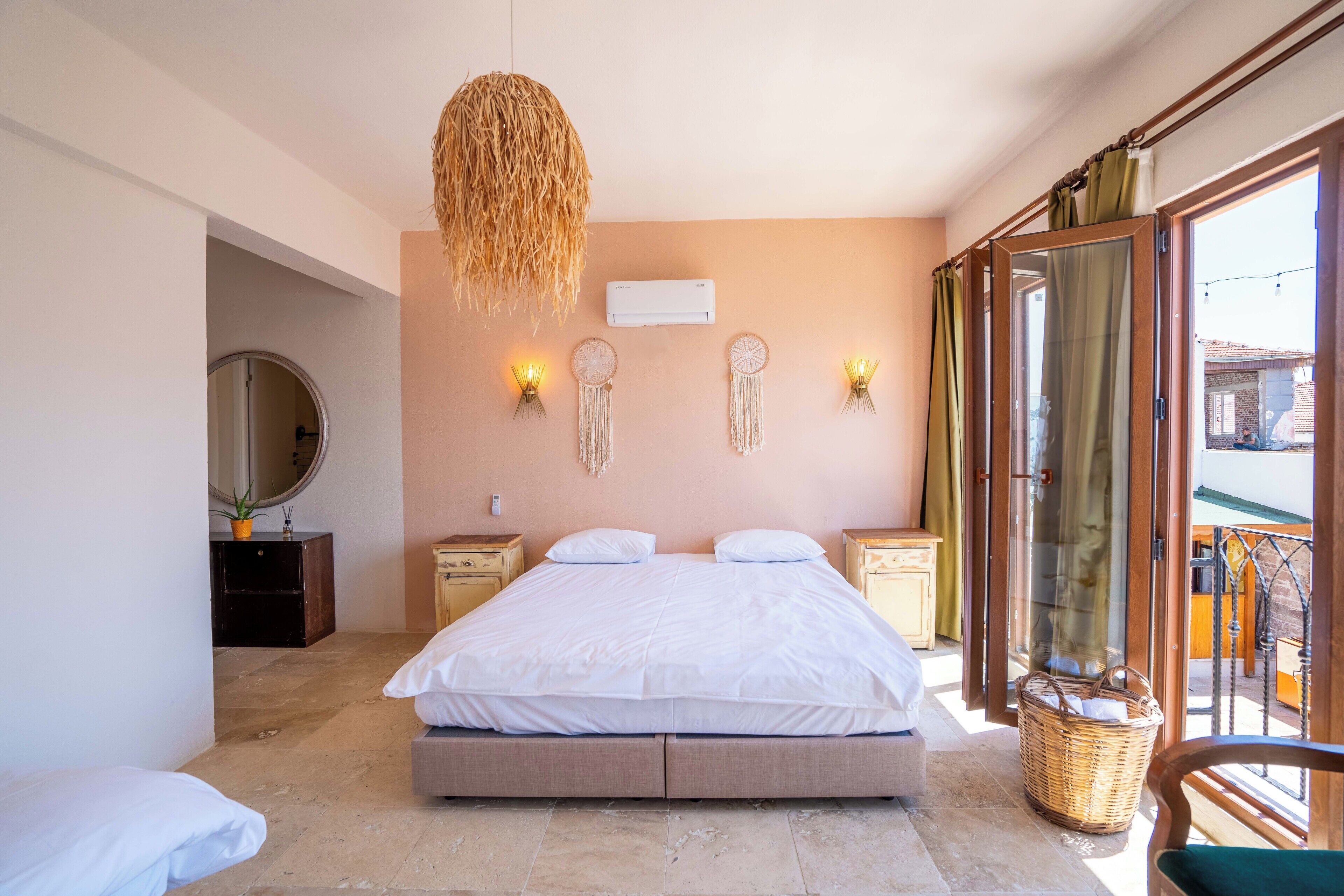 Un dormitorio con una cama grande, mesitas de noche, una lámpara colgante, un espejo y vistas a través de una puerta de cristal.