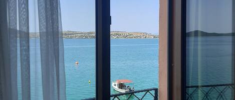 A balcony with a view of a calm sea, a boat, and a distant shoreline.