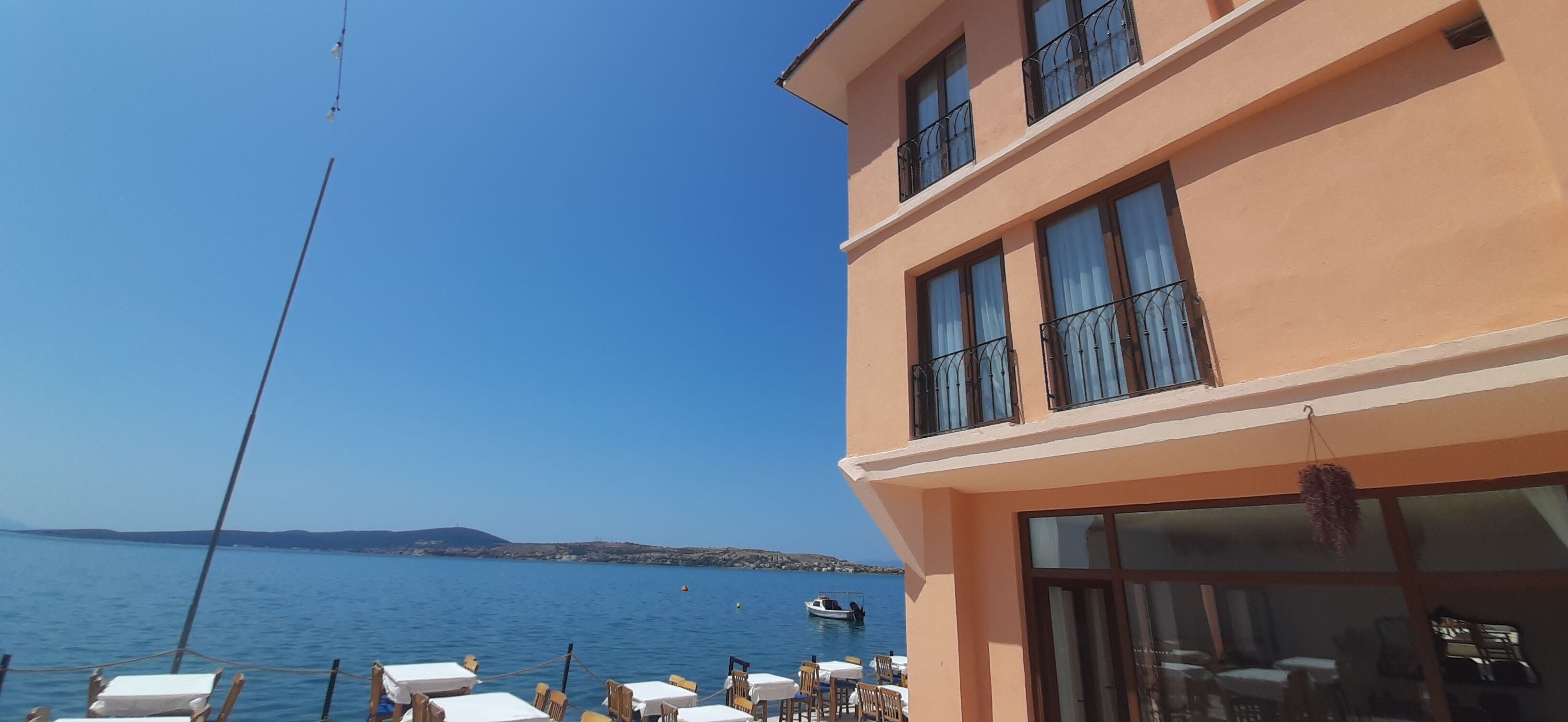 A building with a balcony overlooking a body of water, a clear sky, and a distant shoreline.