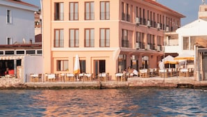 A multi-story building with a red-tiled roof, large windows, and outdoor seating with umbrellas. - Casalyma Ayvalık (Ayvalik)