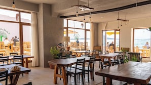 A restaurant with wooden tables and chairs, large windows with views of the sea, and hanging light fixtures. - Casalyma Ayvalık (Ayvalik)