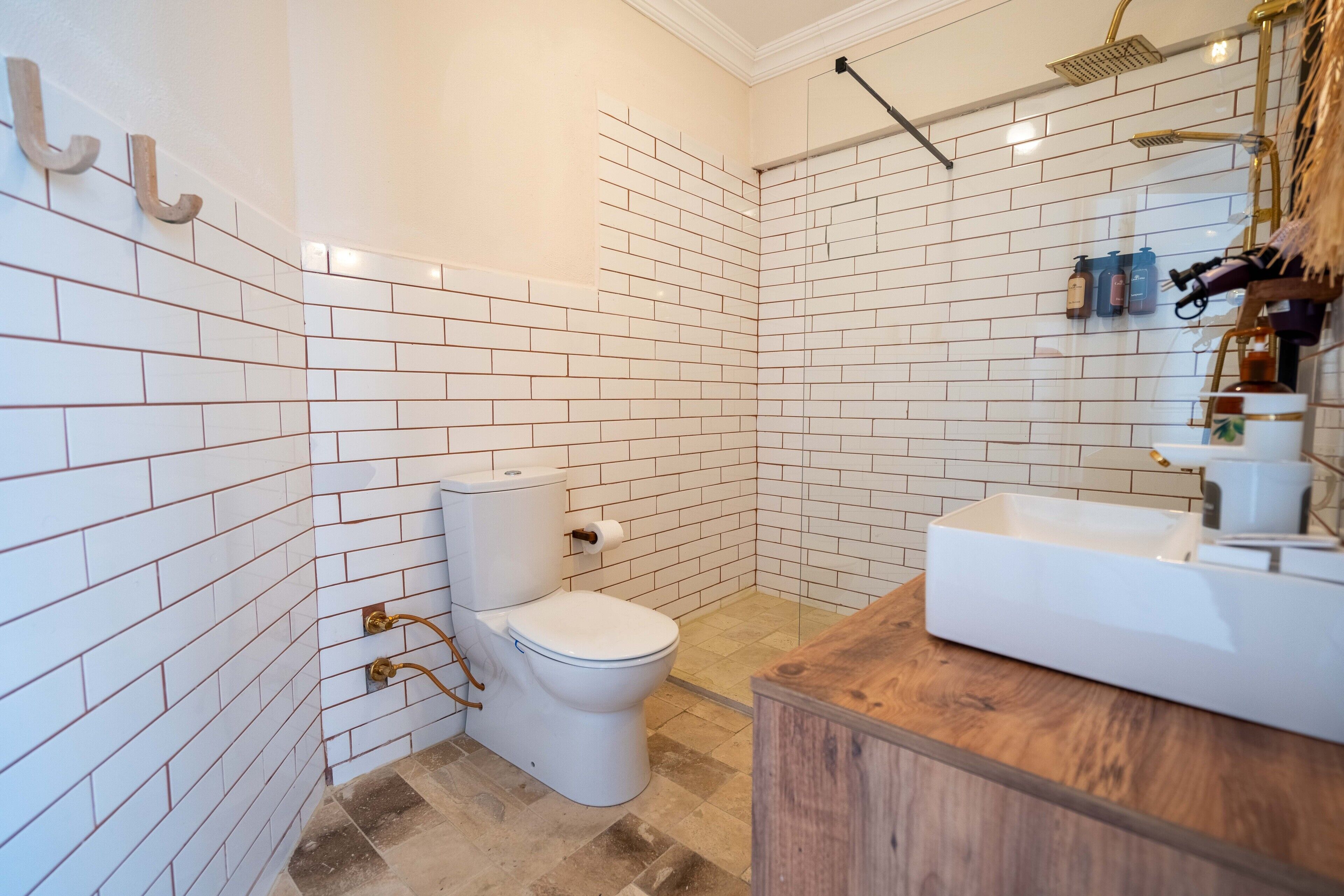 Un baño con azulejos blancos tipo metro, inodoro, ducha y tocador de madera con lavabo.