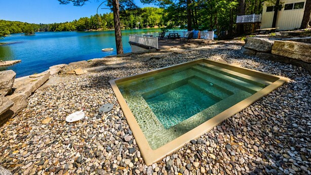 A swimming pool with a pebble surround, a wooden deck, and a lake view. - Hot Tub| Sauna| Arbutus Lake| Pines| 15 min to TC! (Traverse City)