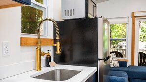 A compact kitchen with a modern design, featuring a stainless steel sink, a black refrigerator, and a gold faucet. - Hot Tub| Sauna| Arbutus Lake| Pines| 15 min to TC! (Traverse City)