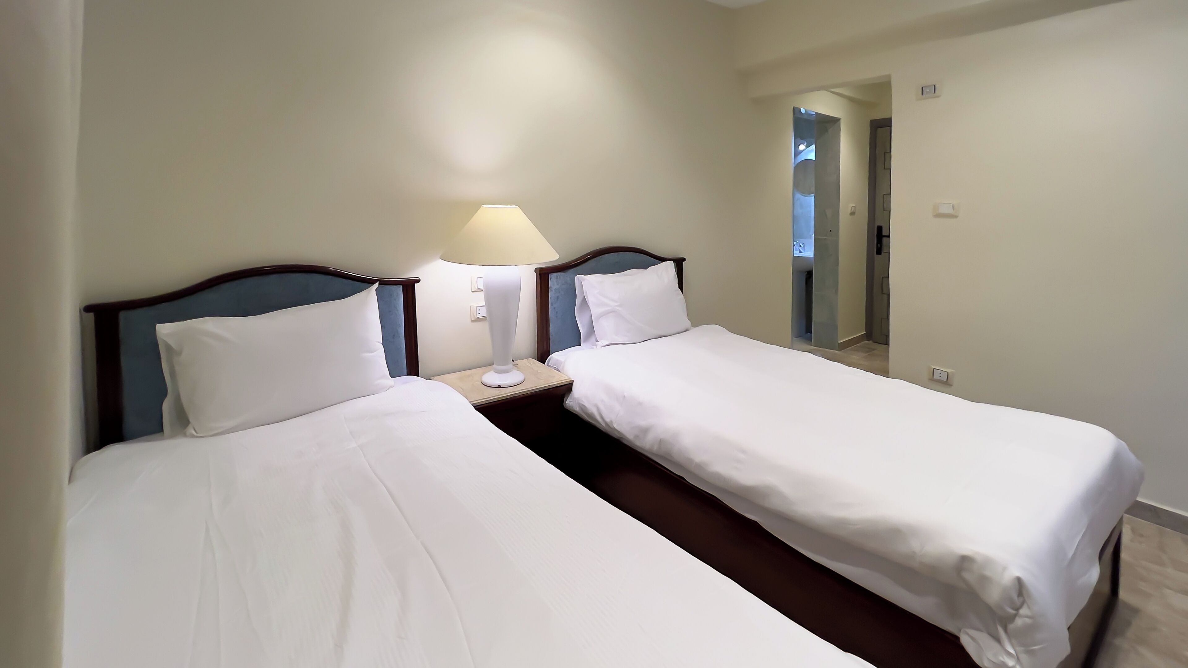 A hotel room with two single beds, a nightstand with a lamp, and a mirror on the wall.