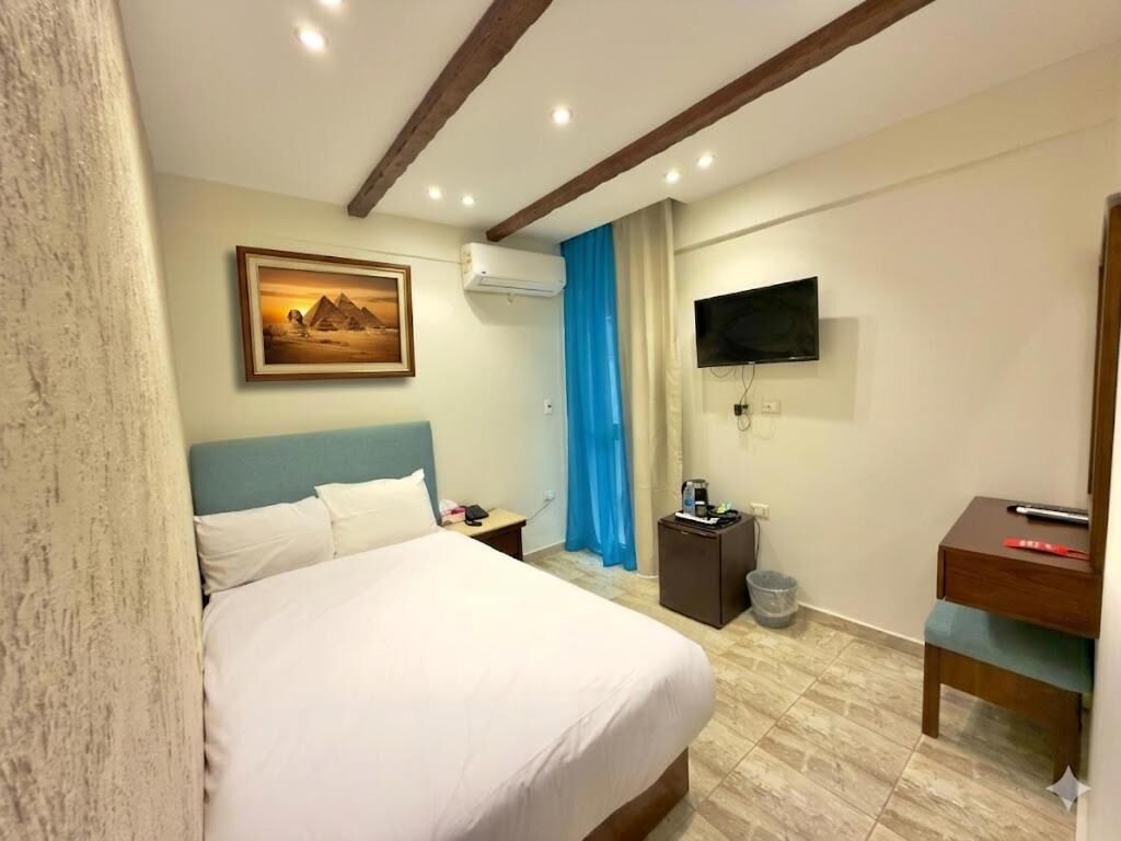 A hotel room with a bed, a desk, a television, and a painting on the wall.
