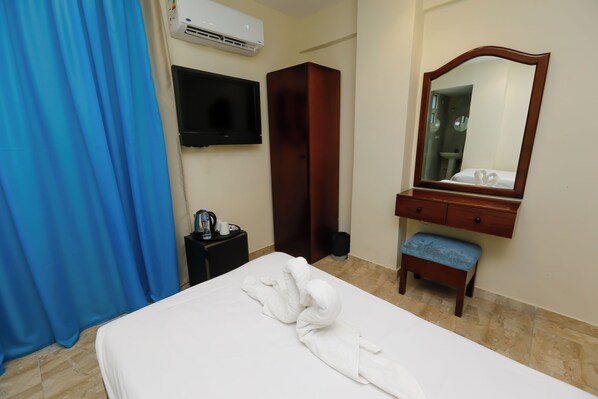 A hotel room with a bed, a wooden bench, a mirror, a wardrobe, a TV, and a trash bin.
