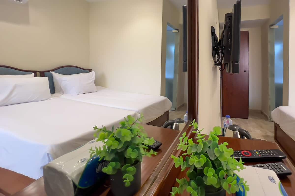 A hotel room with a bed, a desk with a plant, a remote control, and a water bottle.