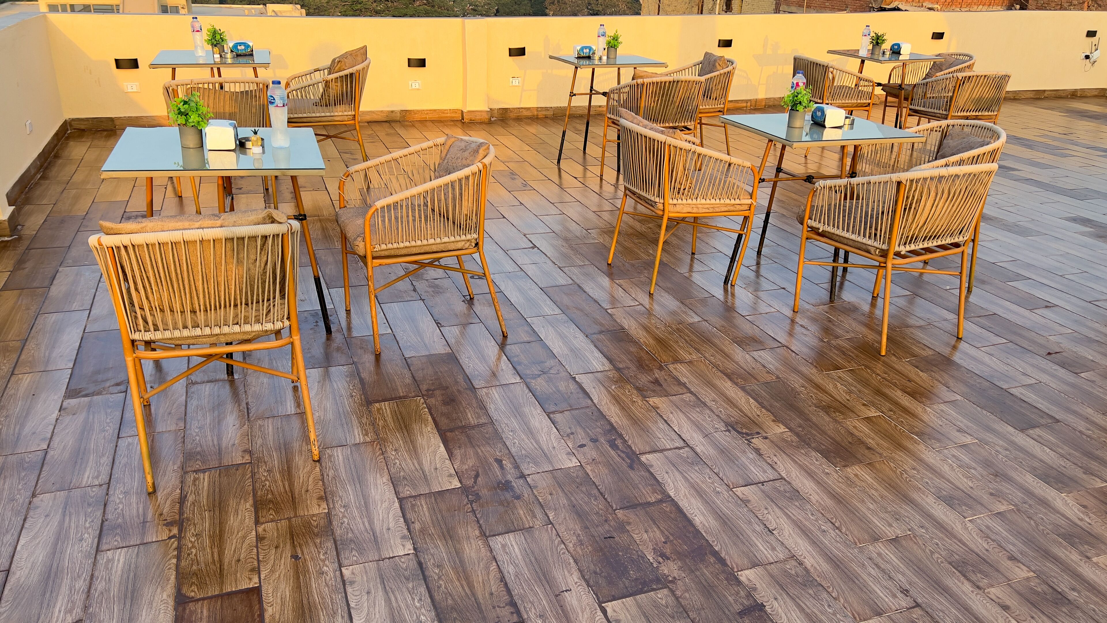 A rooftop terrace with wooden flooring, wicker furniture, and glass tables.