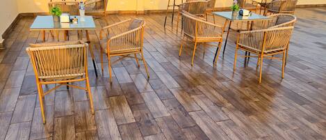 A rooftop terrace with wooden flooring, wicker furniture, and glass tables.