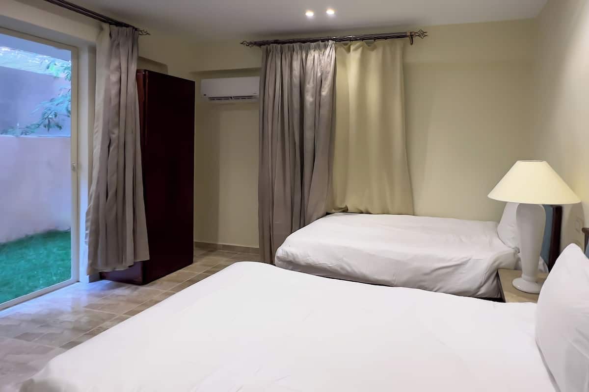 A hotel room with two beds, a lamp, and an air conditioning unit.