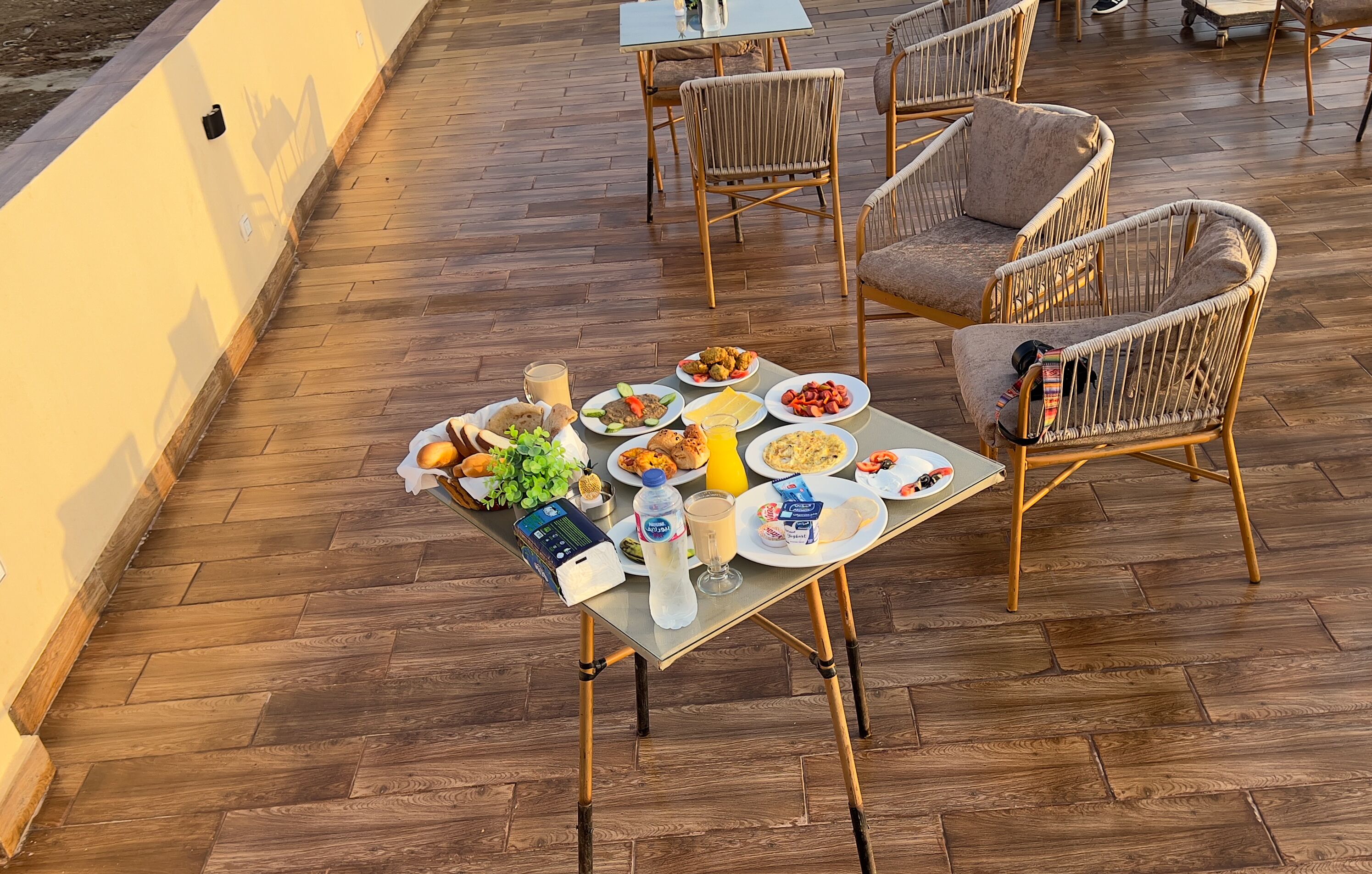 An outdoor dining area with wicker chairs and a table set with various dishes, drinks, and a laptop.