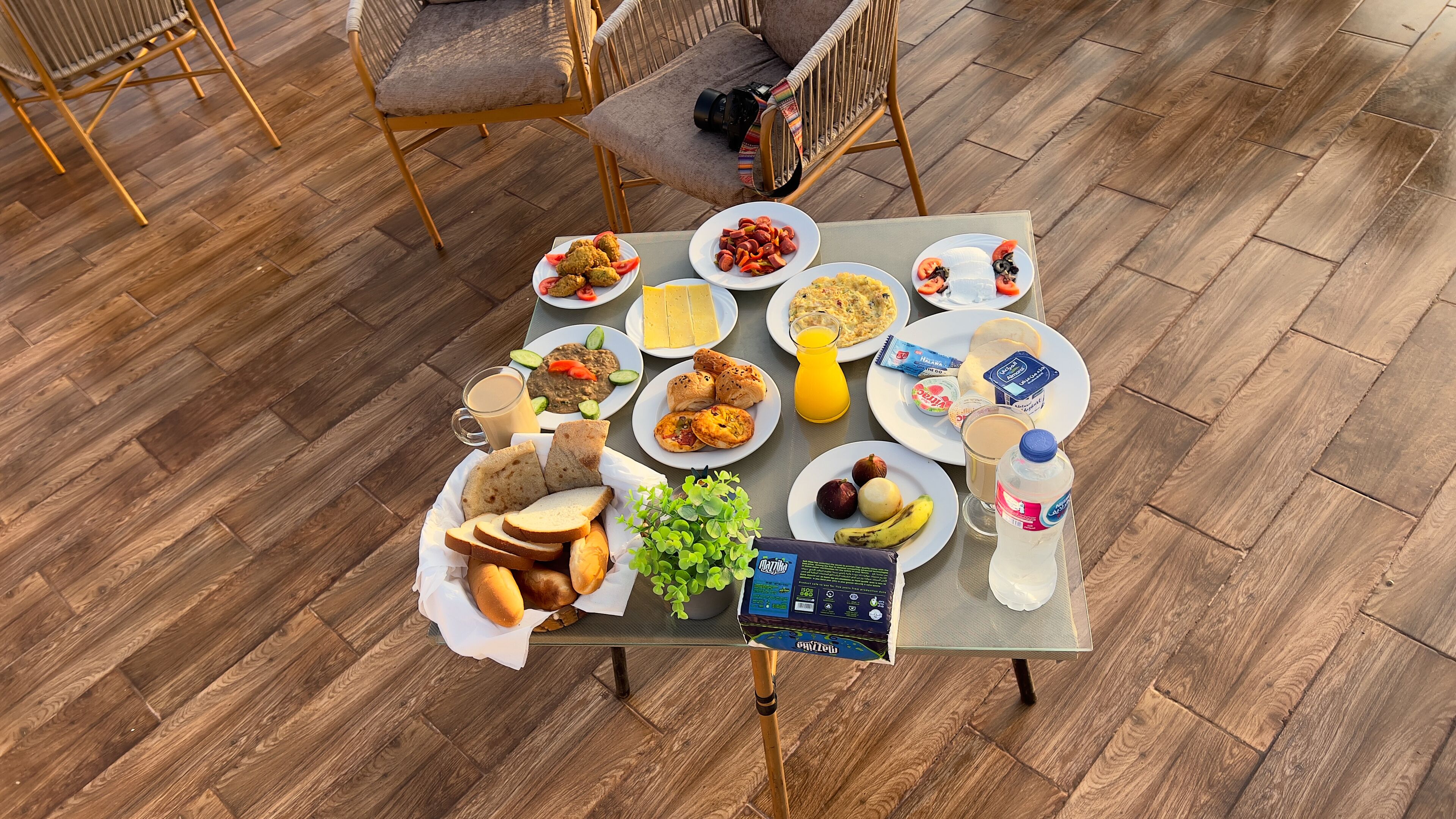A dining table with various food items and drinks, surrounded by wicker chairs.