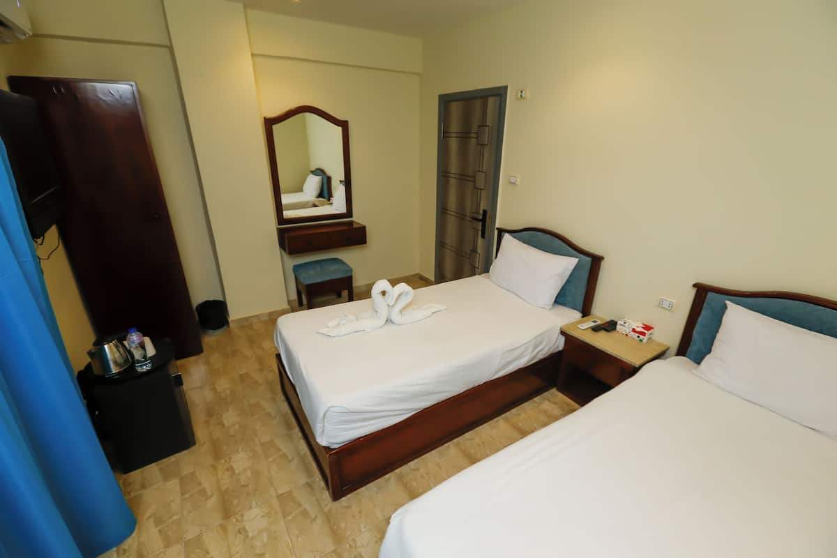 A hotel room with two beds, a wooden wardrobe, a mirror, and a small table with a remote control.