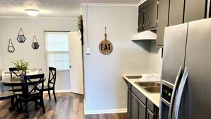 A modern kitchen with a stainless steel refrigerator, wooden flooring, and a dining area with a table and chairs. - Greenhill Boutique Suites (Newport News)