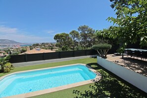 Une piscine rectangulaire à l’eau d’un bleu limpide, entourée d’un mur blanc et d’une pelouse verdoyante.