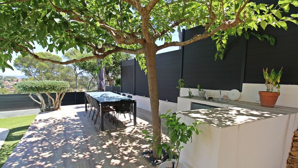 A patio with a table and chairs, a potted plant, and a built-in barbecue grill.