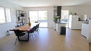 A modern kitchen with a wooden dining table, black chairs, and a black trash bin.