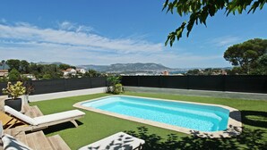A swimming pool with a view of distant mountains, surrounded by artificial grass and wooden lounge chairs.