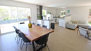 A modern open-plan living and dining area with a wooden dining table, black chairs, a grey sofa, and a kitchen in the background.