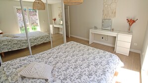 A bedroom with a large bed, a desk, a mirror, and a hanging light fixture.