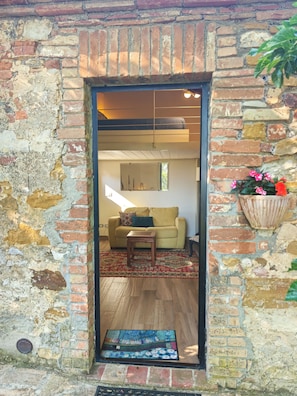 A doorway leading to a living area with a sofa, a small table, and a decorative rug. - "The Grain" (Trequanda)