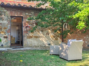 A rustic stone building with a wooden door, a wicker sofa, and a hanging light fixture. - "The Grain" (Trequanda)