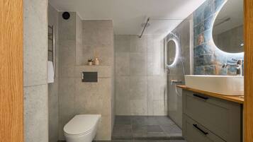 Un baño moderno con inodoro, ducha y tocador con espejo.