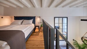A bedroom with a bed, a small table with a plant, and a view of the outside through a window. - Queen Barbora Central Lofts (Kaunas)