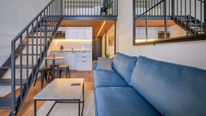A modern apartment with a staircase, a living area with a blue sofa, a dining table, and a kitchen. - Queen Barbora Central Lofts (Kaunas)