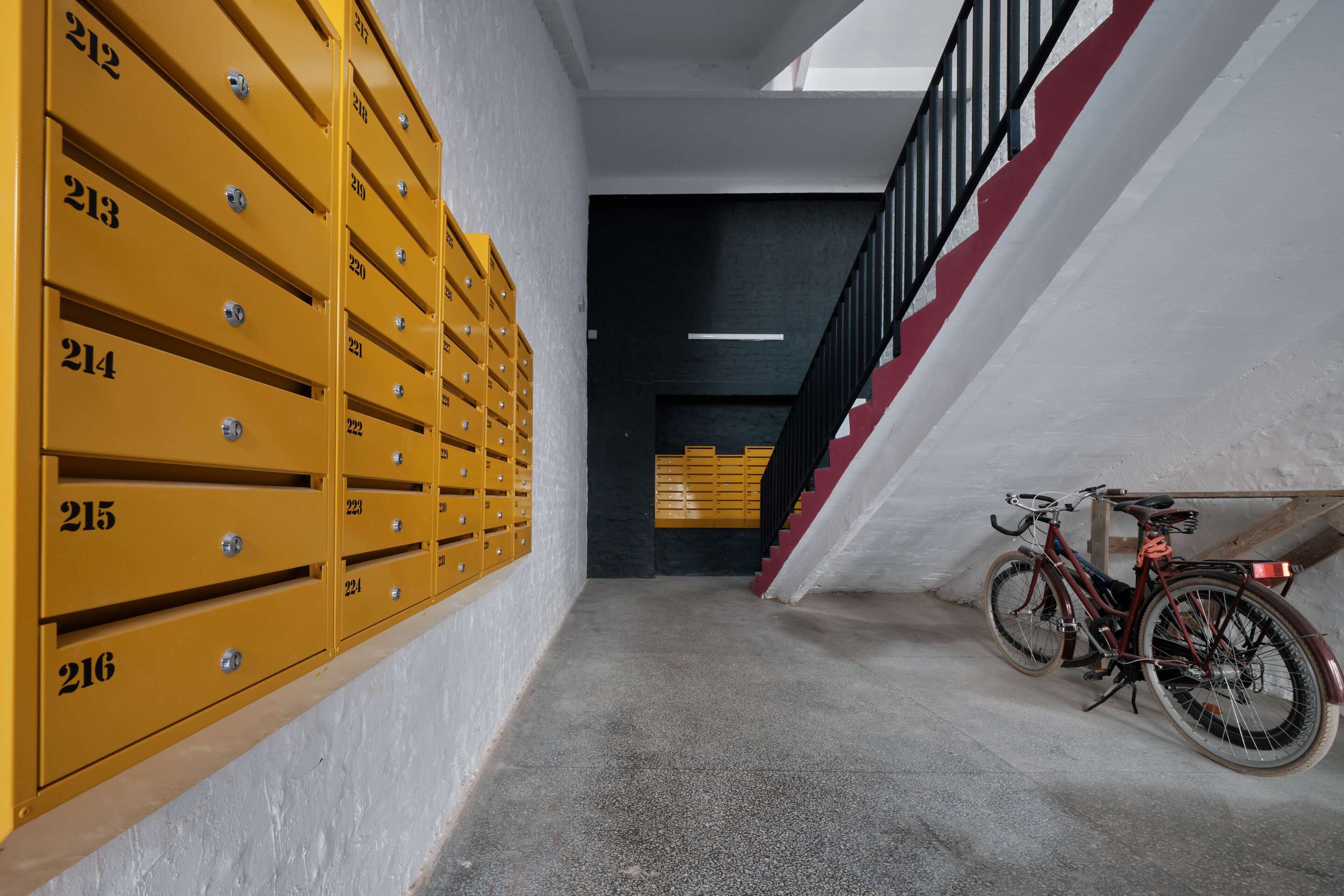 A hallway with numbered yellow mailboxes and a bicycle parked near a staircase.