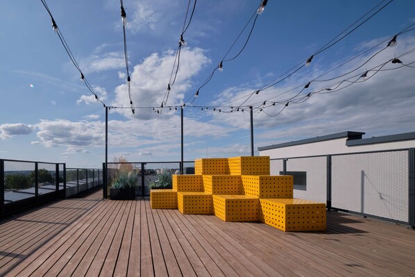 A rooftop deck with wooden flooring, yellow seating, and string lights against a clear sky. - Queen Barbora Central Lofts (Kaunas)