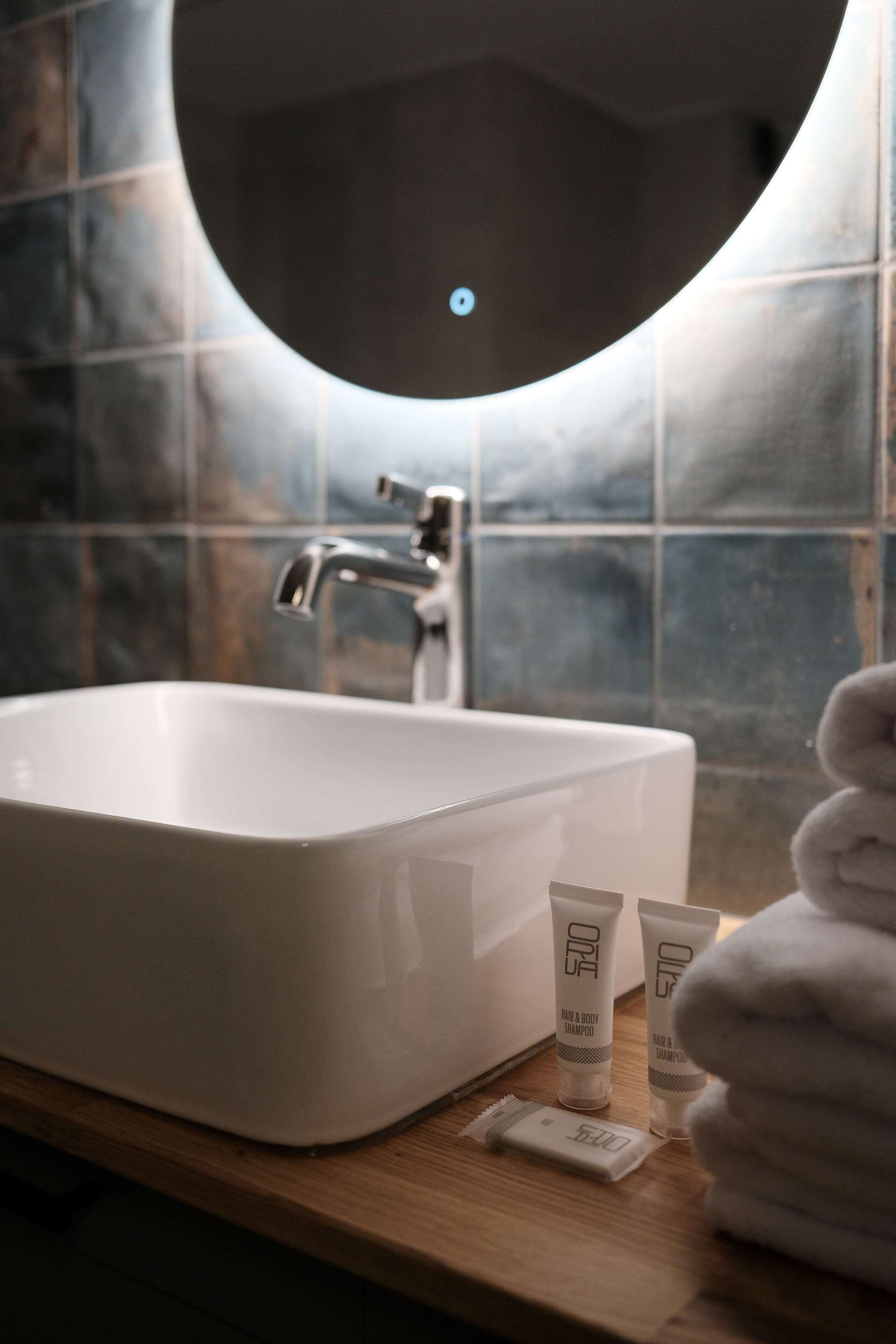 Un bany amb un lavabo blanc, un mirall rodó i productes de tocador al taulell.